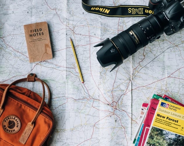 unsplash - Annie Spratt - appareil photo sac à dos bloc notes et livrets sur une grande carte - top 5 des city trips à faire absolument