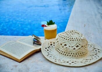 pexels-enginakyurt-lunette de soleil et chapeau et livre et cocktail au bord d'une piscine-8 vêtements indispensables pour slay en vacances