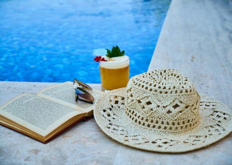 pexels-enginakyurt-lunette de soleil et chapeau et livre et cocktail au bord d'une piscine-8 vêtements indispensables pour slay en vacances