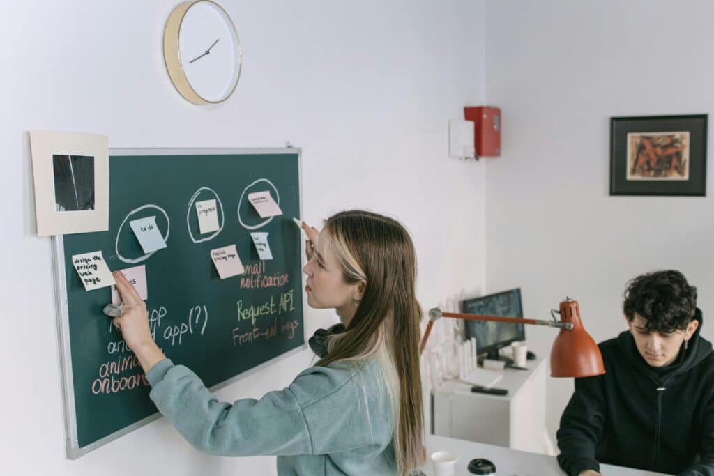 pexels-ivan-samkov-jeune travailleuse qui écrit sur un tableau avec une équipe-Comment mettre en avant ses compétences pour le monde du travail ?