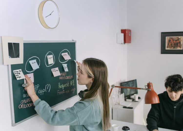 pexels-ivan-samkov-jeune travailleuse qui écrit sur un tableau avec une équipe-Comment mettre en avant ses compétences pour le monde du travail ?