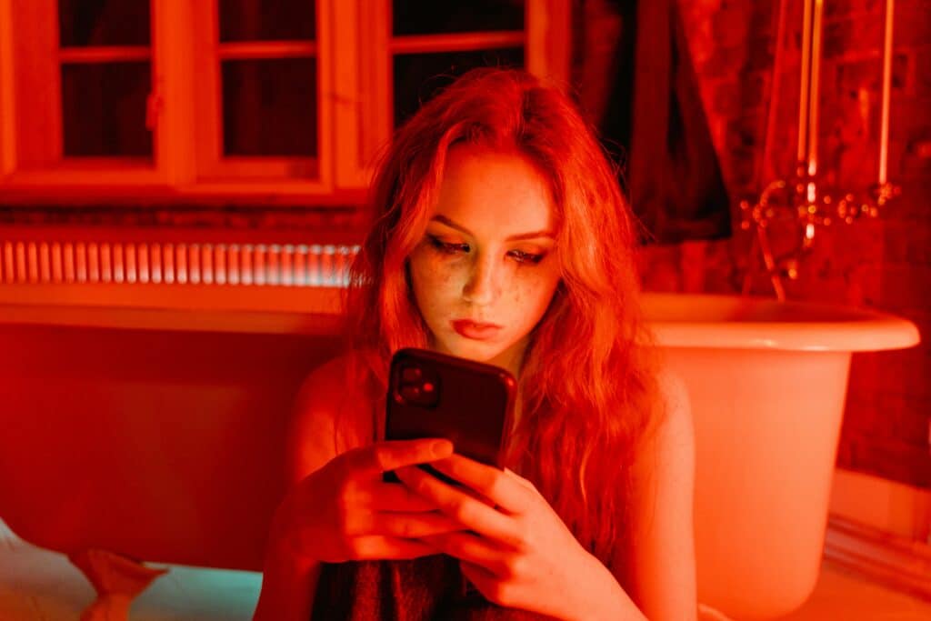 pexels-mart-production-étudiante sur son téléphone dans une ambiance rouge triste-Que faire en Belgique si on est victime de revenge porn ?