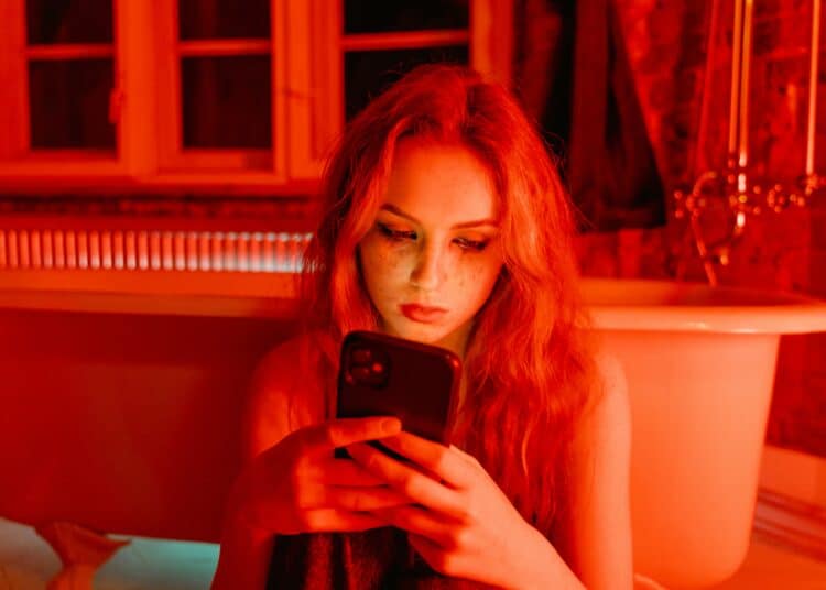 pexels-mart-production-étudiante sur son téléphone dans une ambiance rouge triste-Que faire en Belgique si on est victime de revenge porn ?